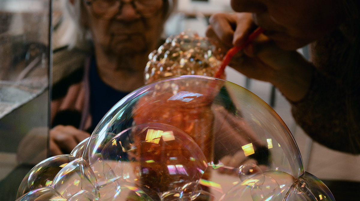 Personne âgée en fond et en premier plan une personne qui souffle dans une paille et faire ressortir des bulles colorées