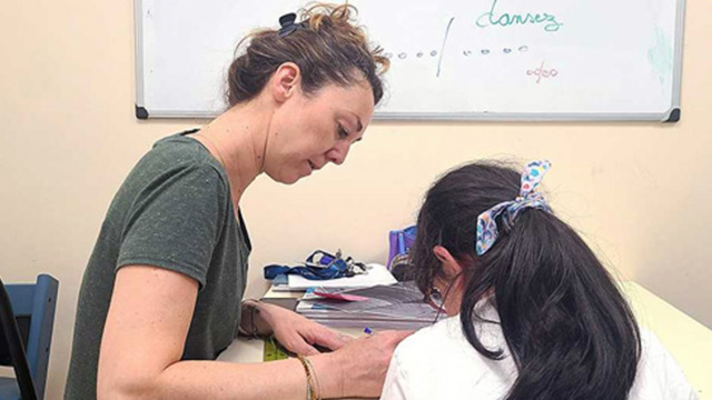 enseignante de profil en train d'écrire et élève de dos au cheveux longs et noirs