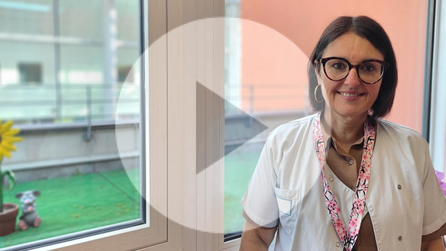 Cadre de santé en blouse blanche devant une fenêtre souriante et portant des lunettes