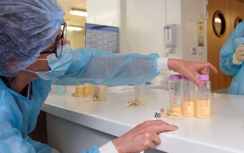 Professionnelle en blouse qui transfert du lait dans des biberons stériles conditionnés.