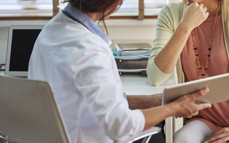 femme médecin en blouse montrant quelque chose sur une tablette à une autre femme (patiente)