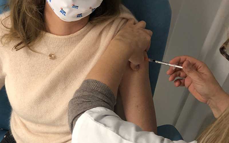 Une jeune femme dont on ne voit pas la tete et qui porte un masque de protection se fait vacciner