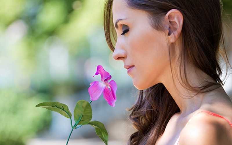 Femme brune aux cheveux longs sentant une fleur violette
