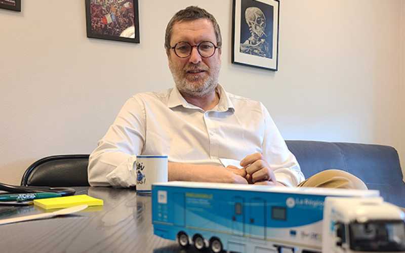 Pr Sébastien Couraud assis à son bureau et le camion de dépistage minitiature