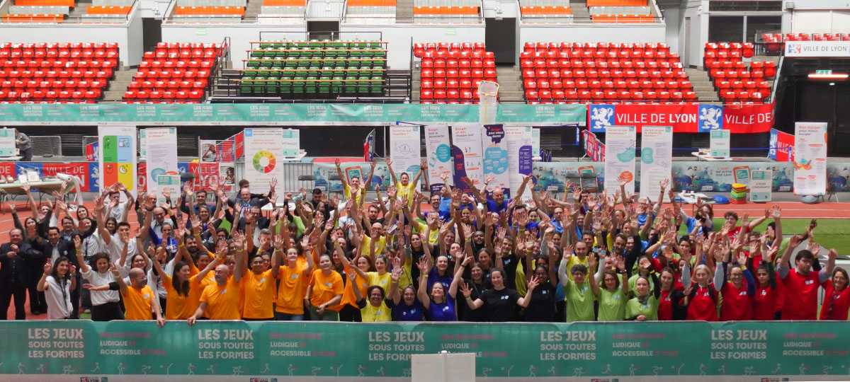 environ 150 personnes posent pour la photo de groupe. elles sont réparties par équipe reconnaissables à la couleur de leur t-shirt : orange, bleu, jaune, rouge...