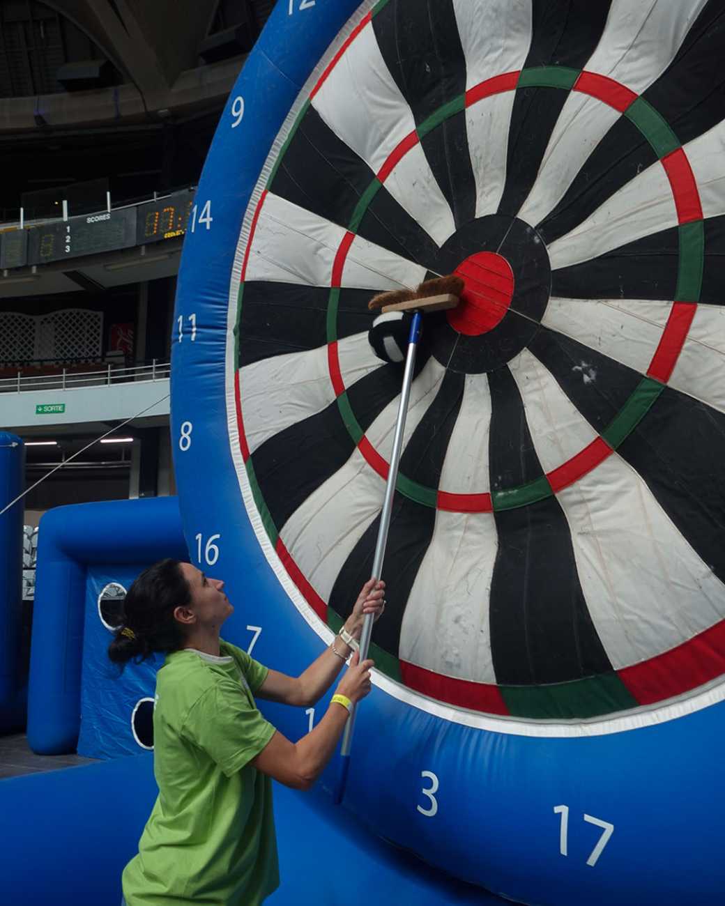 Une femme en t-shirt vert décroche une fléchette scratchée sur une cible géante.