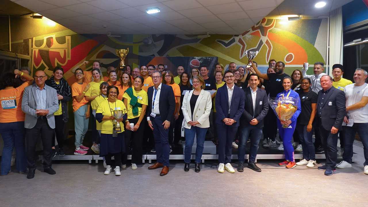 Groupe de personnes souriantes, posant à l'intérieur. Certains ont des t-shirts jaunes, d'autres orange. 