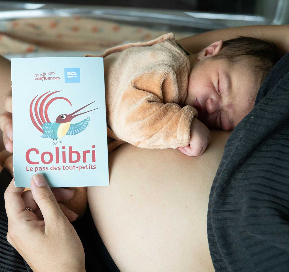 bébé posé sur le ventre de sa mère. La mère tient un flyer avec un oiseau et est inscrit Colibri, le pass des tout-petits