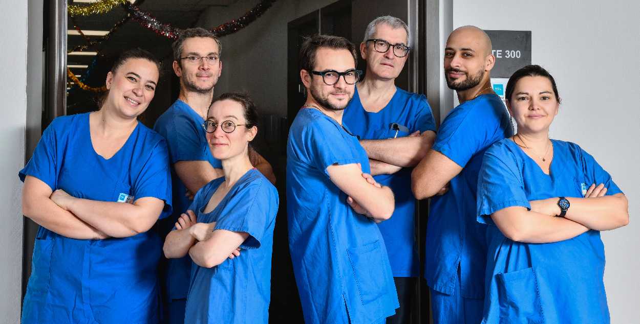 L'équipe de neurochirurgiens est composée de sept personnes, 3 femmes et 4 hommes, ils posent tous, souriants, habillés en bleu, devant un couloir de leur unité 