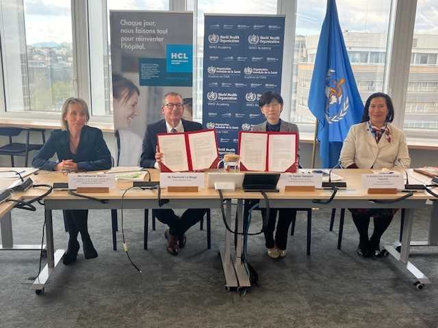 Quatre personnes sont assises derrière une table, elles ont signé un accord de collaboration. Derrière elles, des visuels Hospices Civils de Lyon et OMS.