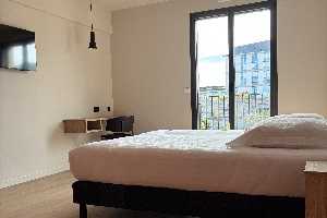 chambre au mur blanc, avec lit, une télévision et une porte fenetre.