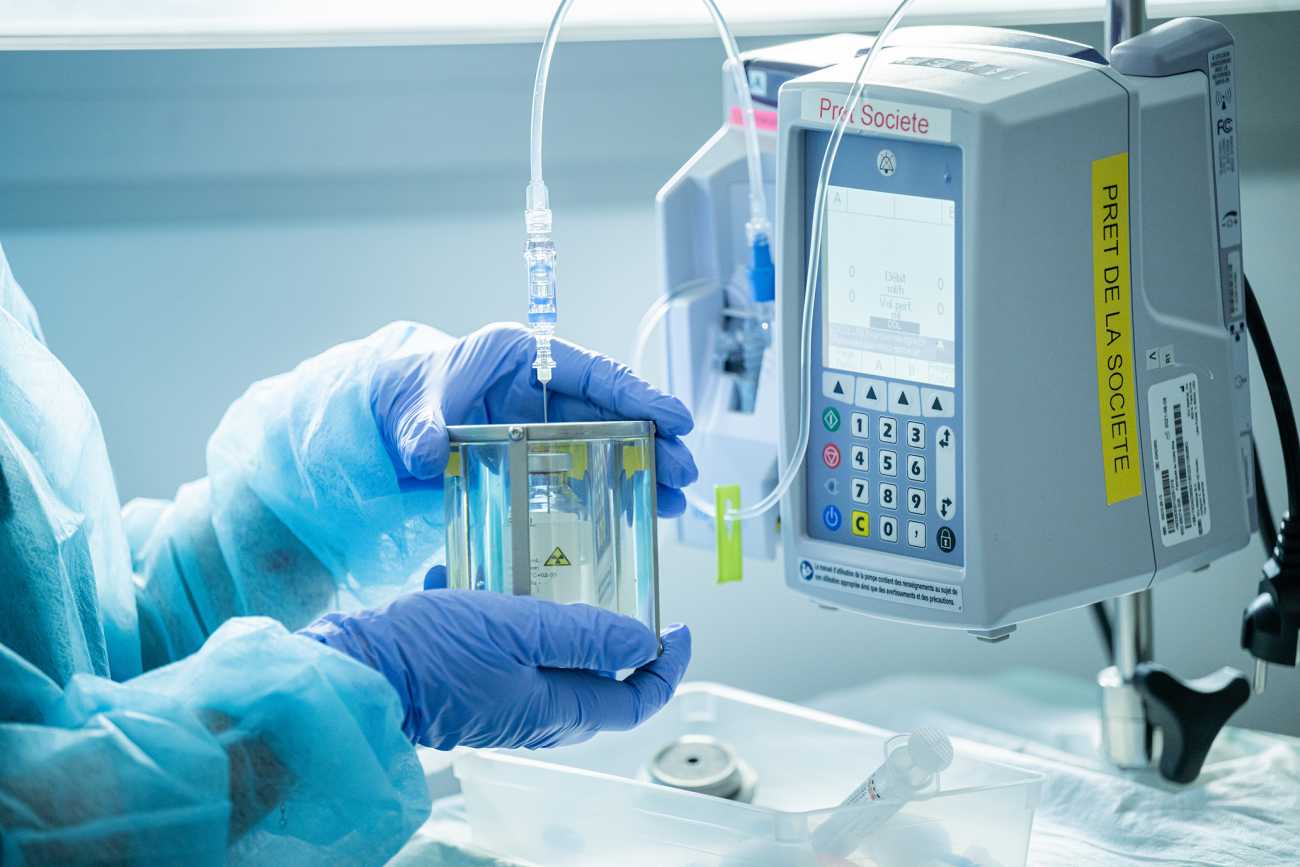 des mains avec des gants bleus tiennent un flacon plein d'un liquide transparent relié à une petite machine