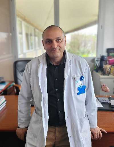 Une homme en blouse blanche se tient devant un bureau. dans son dos, une fenetre.