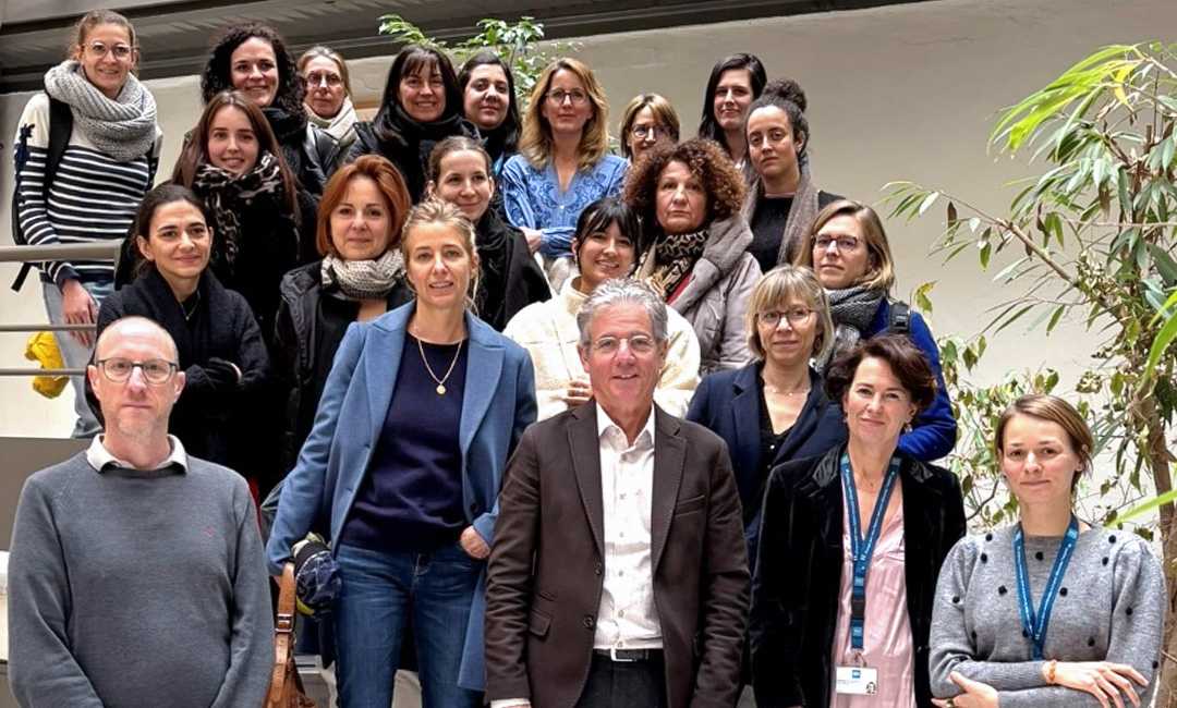 Intérieur. 22 personnes debout sur 4 rangées sur un escalier. 2 personnes à droite portent un tour de cou bleu avec le logo des HCL.