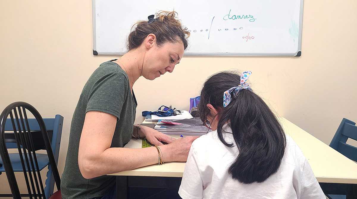 Enseignante assis et enfant de dos aux cheveux longs et noirs en train de travailler et d'écrire