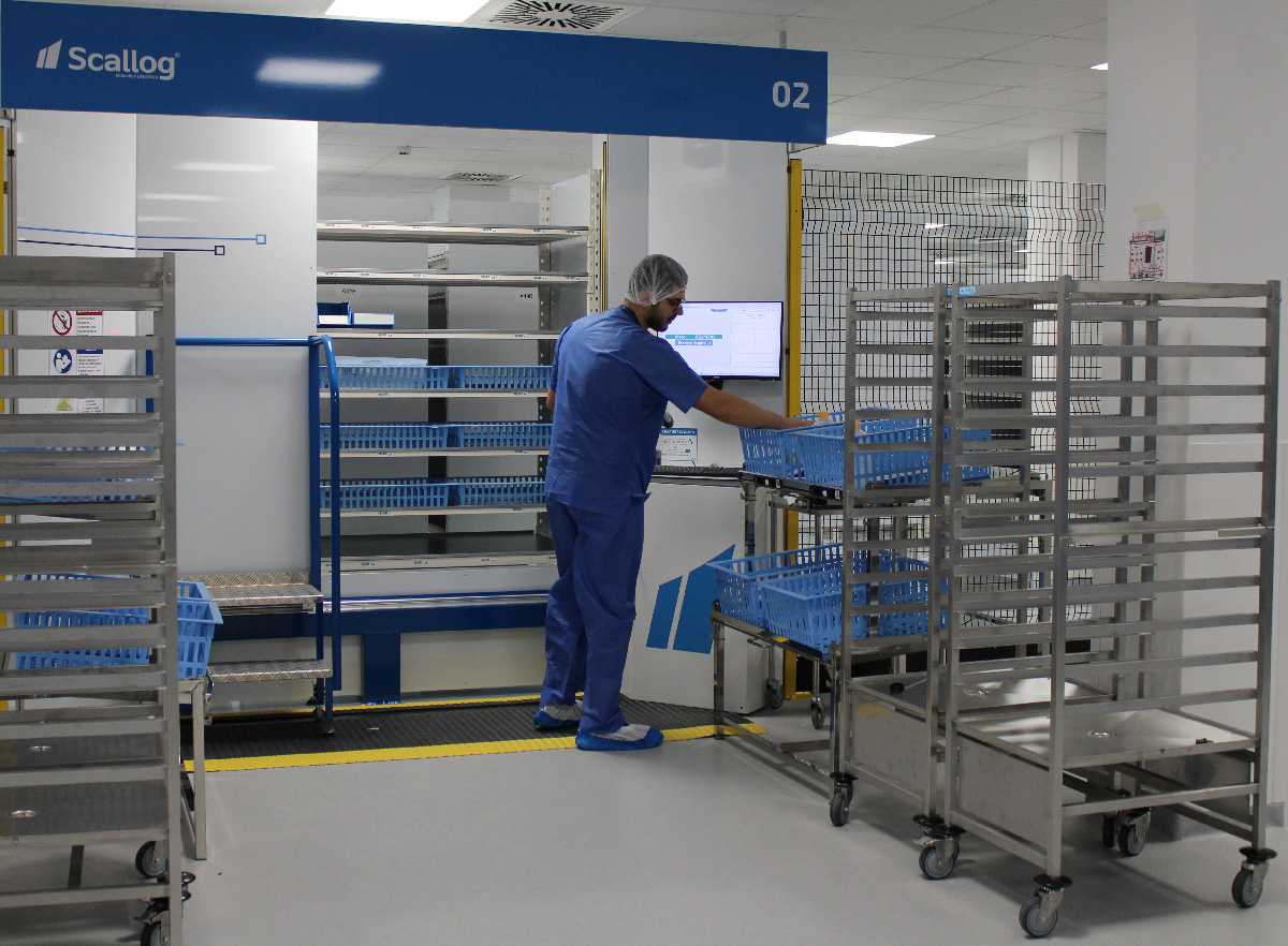 dans un centre logistique hospitalier, un homme habillé en bleu, devant un ordinateur, remplit des casiers bleus