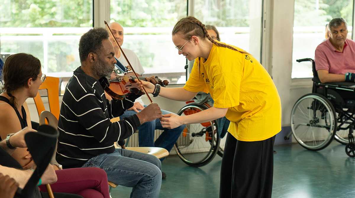 Patient prenant un violon dans la main à l'aide d'une personne de Résonansemble