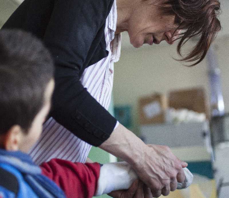 Une femme avec une chemise à rayures et un gilet aide un enfant à se laver les mains