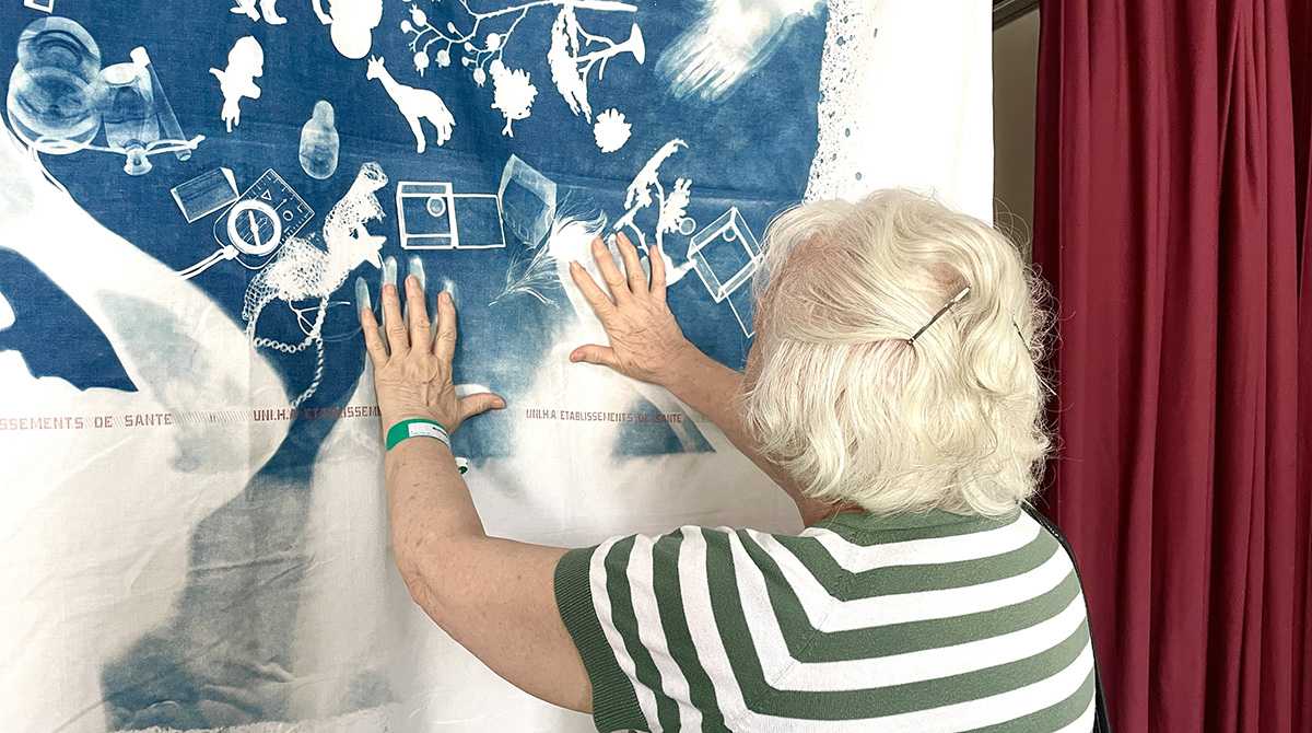 personne âgée de dos avec les mains sur un cyanotype réalisé sur un drap d'hôpital