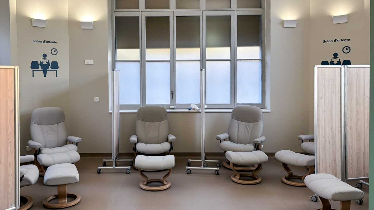 Intérieur. Au mure le texte "Salon d'accueil". Une rangée de fauteuils gris confortables.