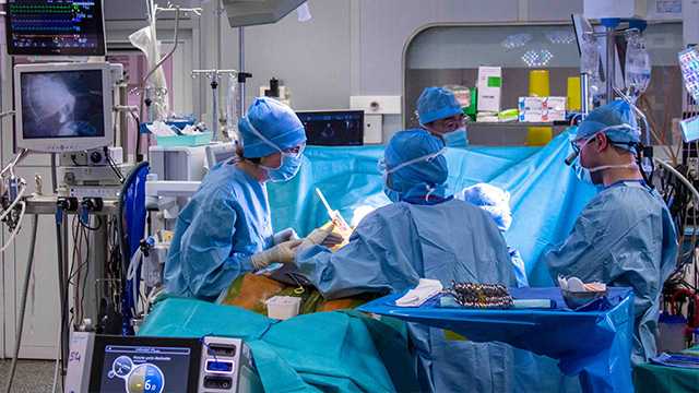 Dans une salle d'opération à l'hopital, quatre chirurgiens en blouses bleues opèrent un patients
