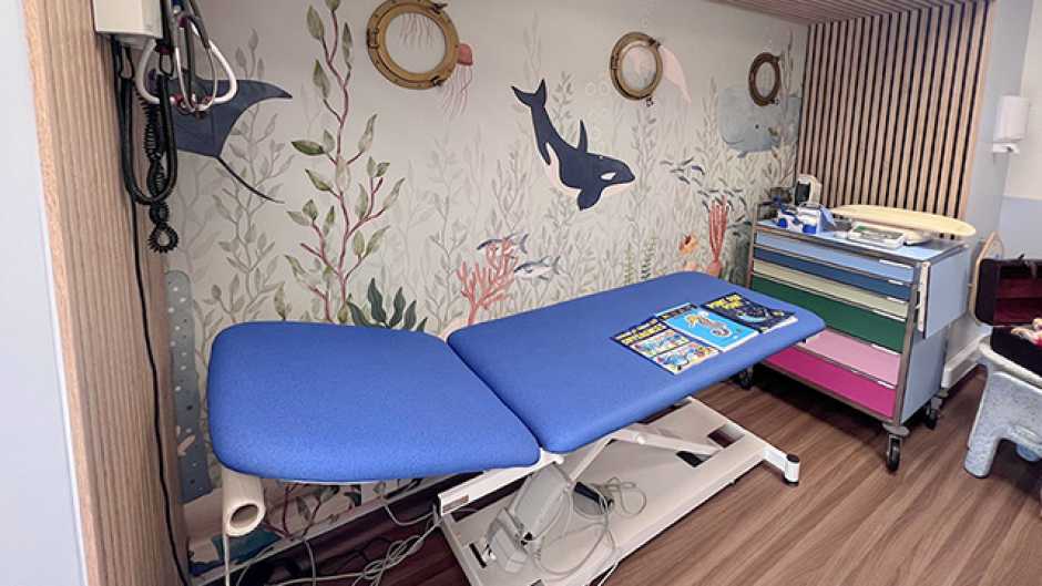 Lit de consultation hospitalier bleu avec un décor sous-marin avec des orques sur le mur du fond et des hublots